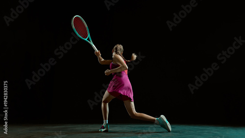 Fotografia Athletic woman tennis player preparing backhand shot in dramatic studio lighting