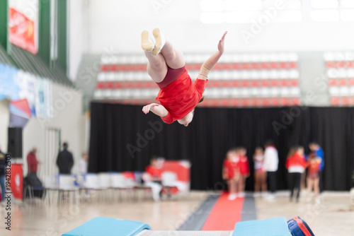 Foto Gymnast performing somersault in indoor gymnastics competition