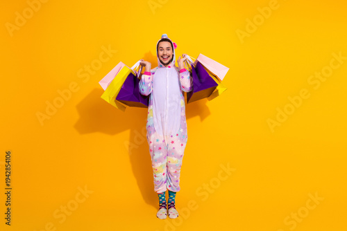 Canvas Print Playful man in unicorn pajama jumpsuit holding colorful shopping bags against a