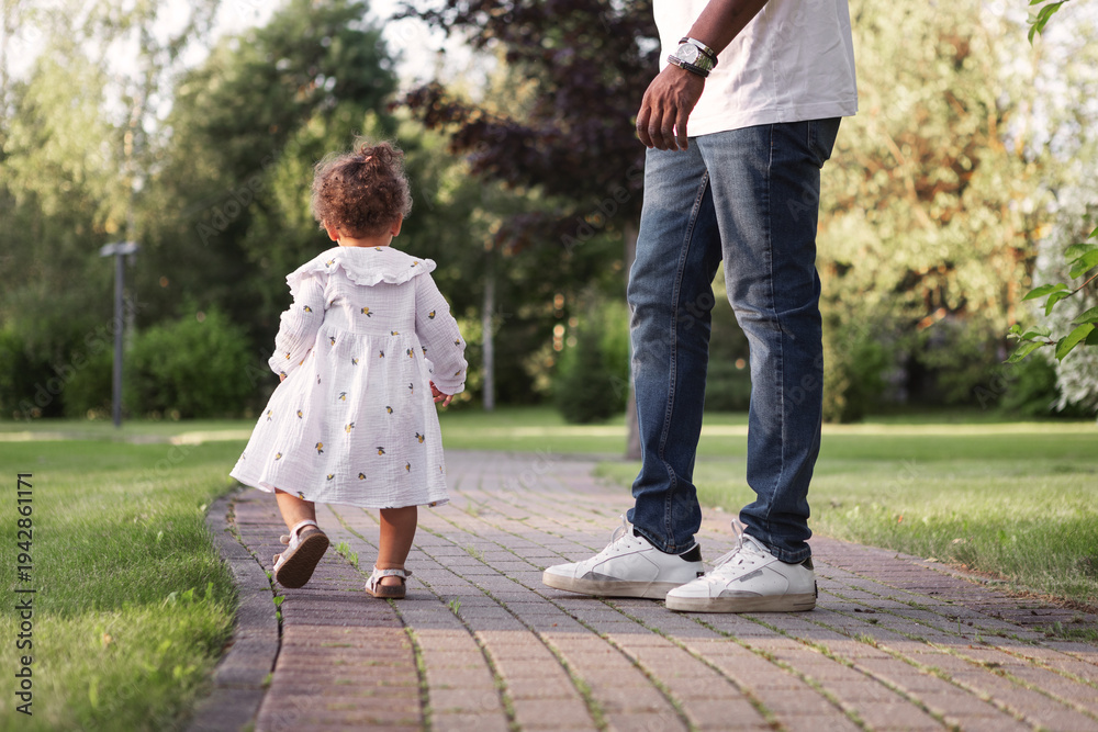 Fototapeta premium Dad with kid. Small child walking away from father during park stroll, back view. Candid family moment outdoors, parenting, independence. Natural lifestyle childhood exploration in summer nature