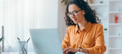 Canvas-taulu A woman sits at a desk in her home office using a laptop