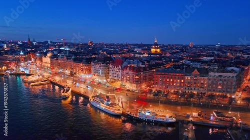 Beautiful boats decorated with lights stand near the waterfront. Aerial view on the gorgeous historical buildings of Stockholm, Sweden in the evening.