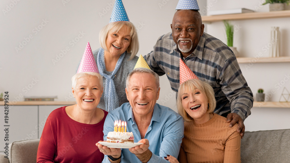 Obraz premium A group of five adults gather in a cozy room to celebrate a birthday. They wear party hats and smile as one person holds a cake with candles. Joy fills the atmosphere.