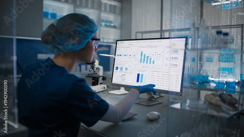 Female scientist in protective clothes and glasses looking at the computer screen. Researching human genetic diseases and DNA test results