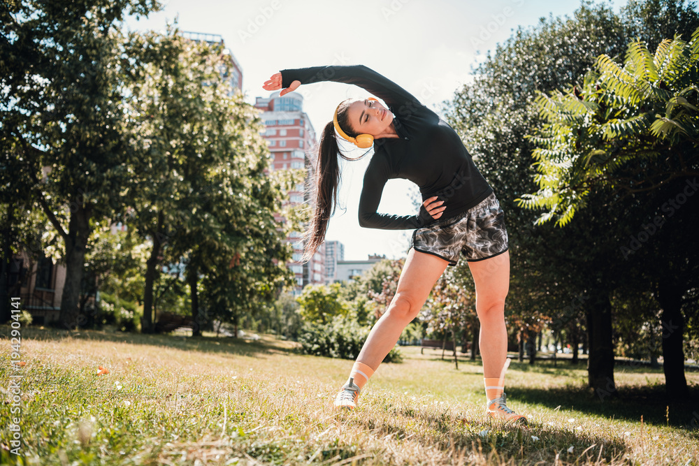 Fototapeta premium Young woman outdoors stretching in the park during a sunny day workout and wellness session