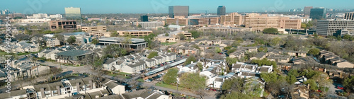 Panorama aerial dense urban housing near Fair Oaks Ave and Holly Hill Dr reveals tightly packed apartments leading toward commercial towers horizon. Brown roofs, parked cars, midtown Dallas, TX