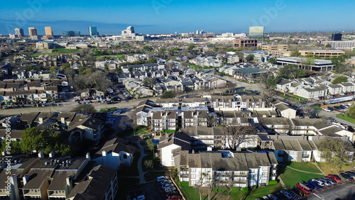 Multifamily–skyline approach near Fair Oaks Ave, Pineland Dr highlights residential clusters extending toward rising office buildings. Light exteriors, patterned roofs, muted foliage rest, Dallas