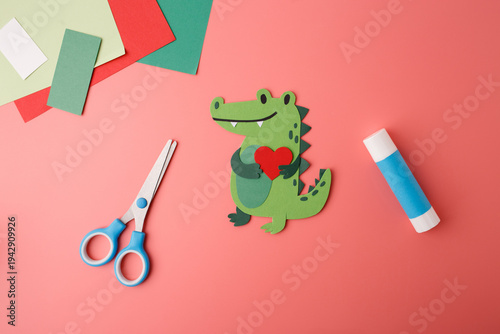Cute paper alligator character with heart symbol, scissors and glue stick. Ideal for childrens dental clinics, pediatric therapy, toy stores, nursery decor, and creative advertising campaigns