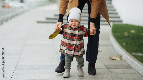Toddler learning to walk outside with parent supporting hands on a chilly autumn day
