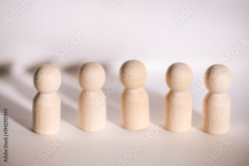Five wooden figurines arranged in a line on a light background, casting soft shadows, showcasing simple design and natural wood texture