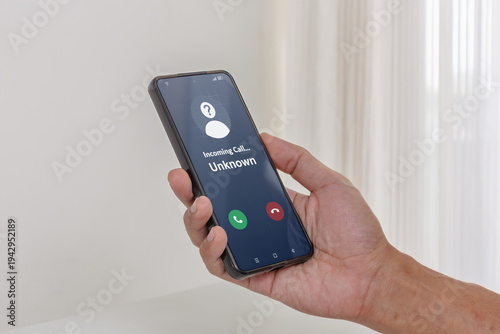 Incoming call from unknown person. Hand holding a smartphone with an incoming call from an unknown number on the screen.