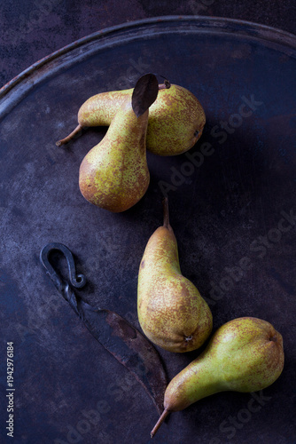 Four green pears 'Abate Fetel' and an old knife on rusty ground
