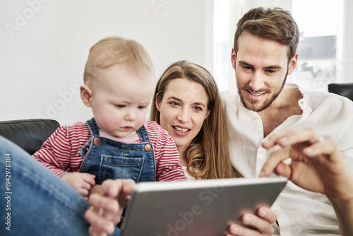Parents with baby girl looking at tablet on couch