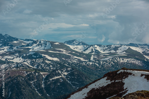 Aerial view to forest hills and big mountain range with snow, sharp rocks, po...