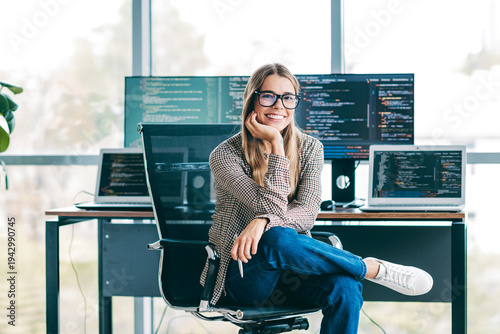 Canvas Print Smiling female software developer sitting in modern office with laptops and mult
