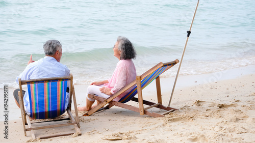 An elderly man and woman smiling brightly while relaxing on the seaside beach.