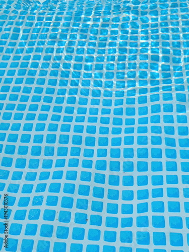 Clear water rippling over a blue swimming pool liner. Geometric square tile pattern distorted by water surface reflections