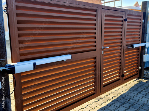 dual-swing gate with built-in pedestrian wicket door, featuring wood-look horizontal louvers linear actuator drive system. Automation Mechanism silver and black arms mounted to gate linear actuators.