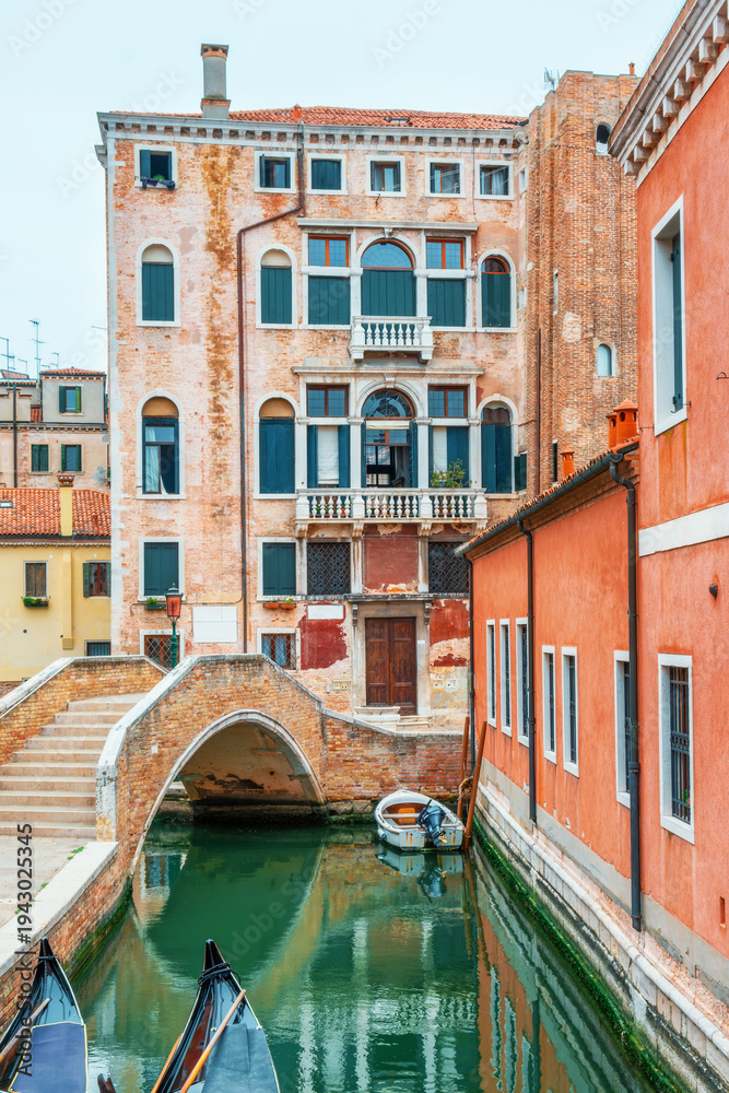 Fototapeta premium Venice canal in old town with historic buildings, small brick bridge and gondolas in traditional Italian cityscape. everyday transport and traditional architecture in the Venetian lagoon city, Italy