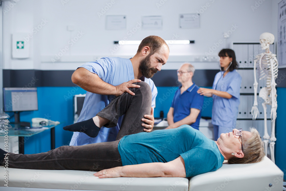 Obraz premium Chiropractor giving assistance to senior patient with knee injury for physical recovery. Woman doing leg exercise with help from medical assistant for osteopathic remedy and treatment.