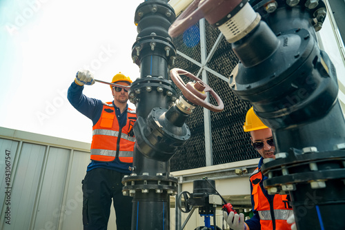 Quadro su tela Industrial workers in safety vests and hard hats performing maintenance on large