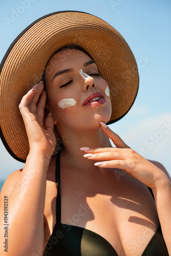 Skin care. Beauty Concept. Young pretty woman applying suncream and touch own face. Female in hat smear sunscreen lotion on skin. Skin Protection and dermatology.
