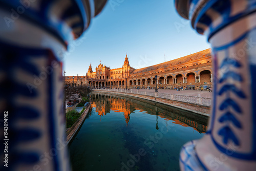 Golden hour Plaza de Espana in Seville shows arcaded galleries, brick towers, ceramic details, and curved canal reflections, with visitors strolling along the promenade.