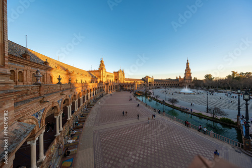 Late afternoon Plaza de Espana view with north tower and fountain in Seville, Spain. Wide angle scene shows arches, canal bridges, azulejo benches, and strolling visitors.