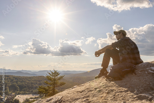 African American man sitting on a rock outcropping after a hike in nature and wilderness taking in a stunning view, Vermont, New England, USA. Thrill and exercise at the top of a mountain.