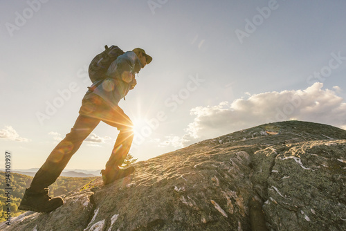 Fotografie African American man hiking and walking in nature up to the summit of a mountain with great views with a backpack