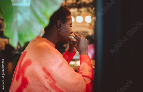 Fotografija Close-up of a smiling young woman holding a fresh burger, ready to eat in a bright and cozy cafe, focusing on food photography, youth culture and real human emotions during leisure time