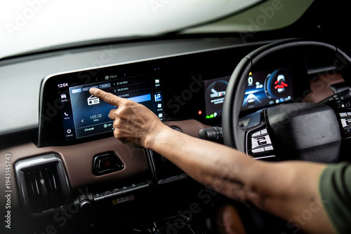 Driver touching infotainment touchscreen to select radio station inside modern vehicle dashboard, digital car entertainment system interface.
