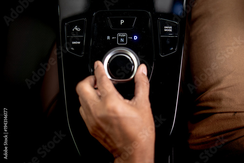 фотографія Driver hand operating rotary gear selector on modern vehicle center console with park reverse neutral and drive transmission controls