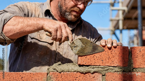 Professional bricklayer building red brick wall using trowel wet cement heavy manual labor construction site masonry industry hard work builder occupation architecture contractor tool