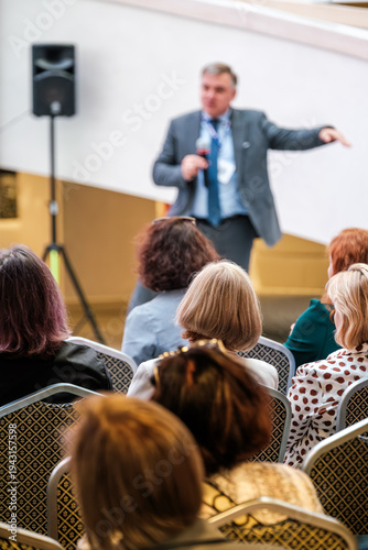 Wallpaper Mural Business speaker delivers presentation to seated audience at professional conference, attendees listen and take notes. Torontodigital.ca
