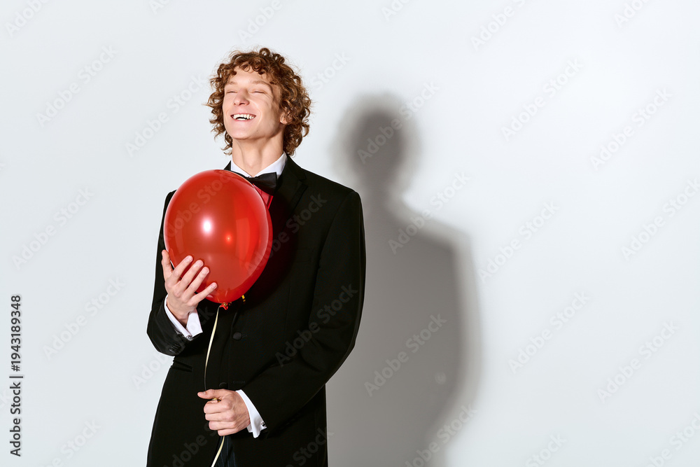 Obraz premium Elegant young man in a tuxedo celebrates with a balloon in a joyful studio setting