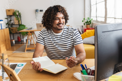 Photos Young adult Indian man student holding notebook while studying at home desk