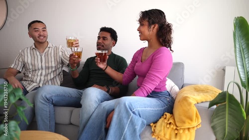 Three happy multicultural friends sitting on a couch, smiling and clinking glasses in a cheerful toast, enjoying a relaxing and joyful gathering together in a cozy living room
