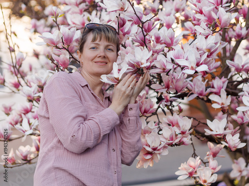 Tableau sur toile Woman gently touching blooming magnolia flowers (Magnolia) in spring garden, soft pink color palette, concept of spring blossom, enjoying nature and seasonal beauty