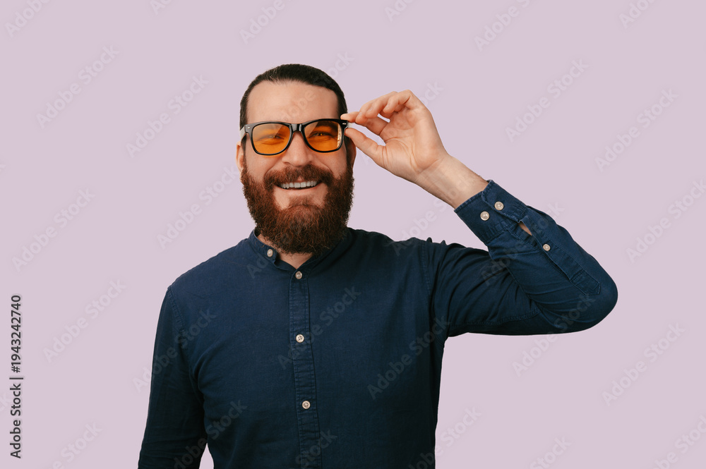 Obraz premium Bearded Man Adjusting Glasses Playful Smile, Studio Headshot On Lavender Background, Amber Tinted Frames,