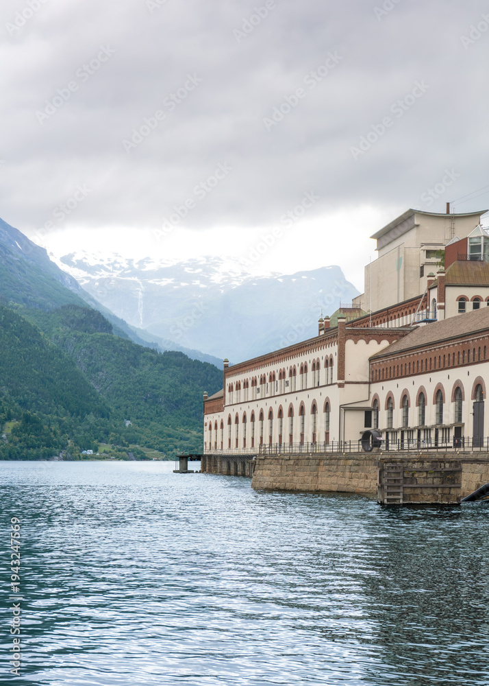Fototapeta premium Western norway energy identity-large power station standing along fjord shoreline in Tyssedal beneath forested mountains, representing regional industrial history, regional development concept