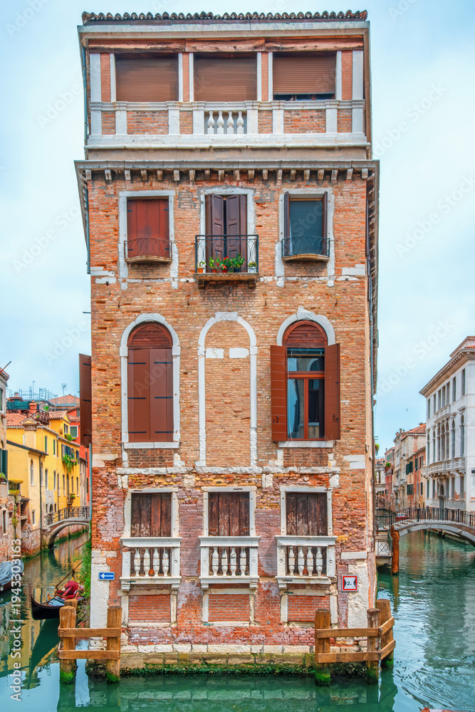 Fototapeta premium Historic Venetian brick building standing between two canals with gondolas in Venice old town, Italy. Italianl architecture. Historic European city. Travel destination. Vertical orientation