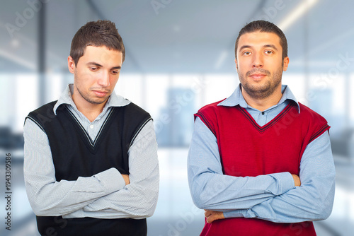 Two men are standing in a room, one wearing a black vest