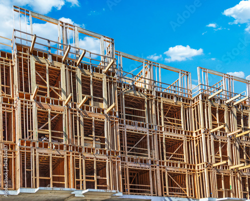 Under construction multi-story residential building with wood frame structure and OSB sheathing against a blue sky