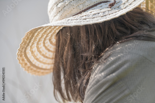 Canvas Print Woman wearing wide straw hat with brown hair falling over shoulder, standing outdoors in soft natural light with blurred green background