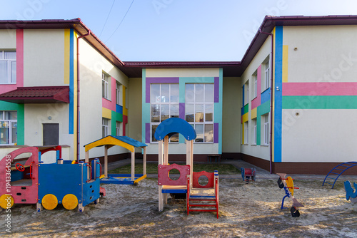 Colorful Kindergarten Courtyard With Playground Equipment. Bright empty kindergarten courtyard featuring playful equipment and a pastel school facade, creating a cheerful outdoor space for early