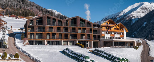 Tableau sur toile Modern alpine lodge in South Tyrol, Italy, with sawtooth roof and balconies sits in a snowy valley near Dolomite peaks, conifer forests, and a chalet as smoke drifts