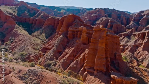Aerial view captures majestic eroded sandstone formations in Konorchek canyons, Kyrgyzstan. Rugged landscape showcases ancient geological beauty under clear sky.