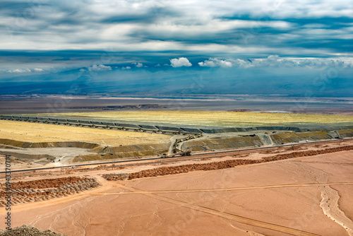 A wide aerial view shows multiple leach pads contained within berms and connected by long, portable conveyor belt systems in a desert mining operation in Chile