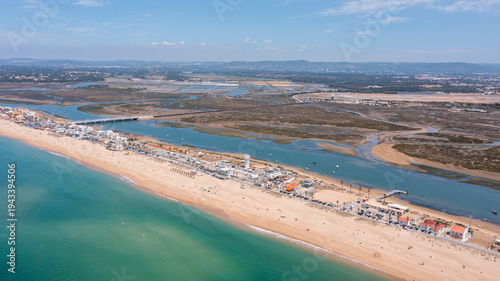 Aerial view shows Praia de Faro with people on the beach and Ria Formosa nearby. The coastline stretches as boats are visible in the water on a clear day